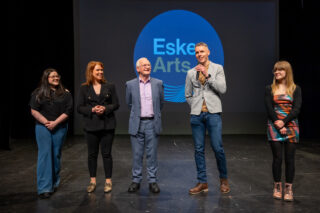 A group of five people standing on a stage, smiling and facing the audience.